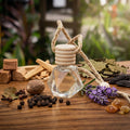 Faceted glass hanging car diffuser bottle filled with Palo Santo and patchouli fragrance oil, surrounded by raw ingredients including black pepper, nutmeg, lavender, and wood chips on a rustic wooden table.